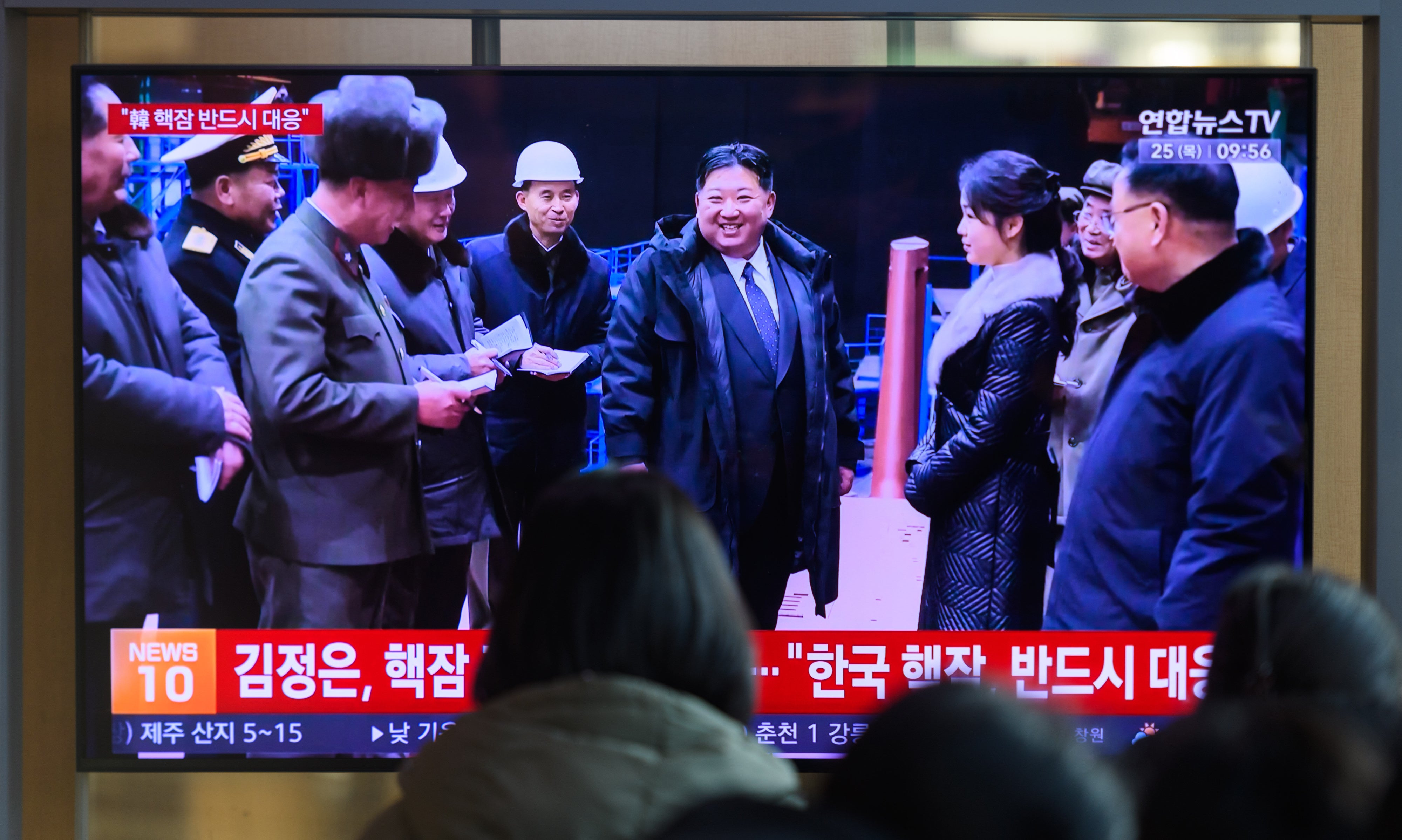 South Koreans in Seoul watch a news broadcast showing North Korean leader Kim Jong Un and his daughter visiting the undisclosed manufacturing site for a nuclear-powered submarine, December 24, 2025.