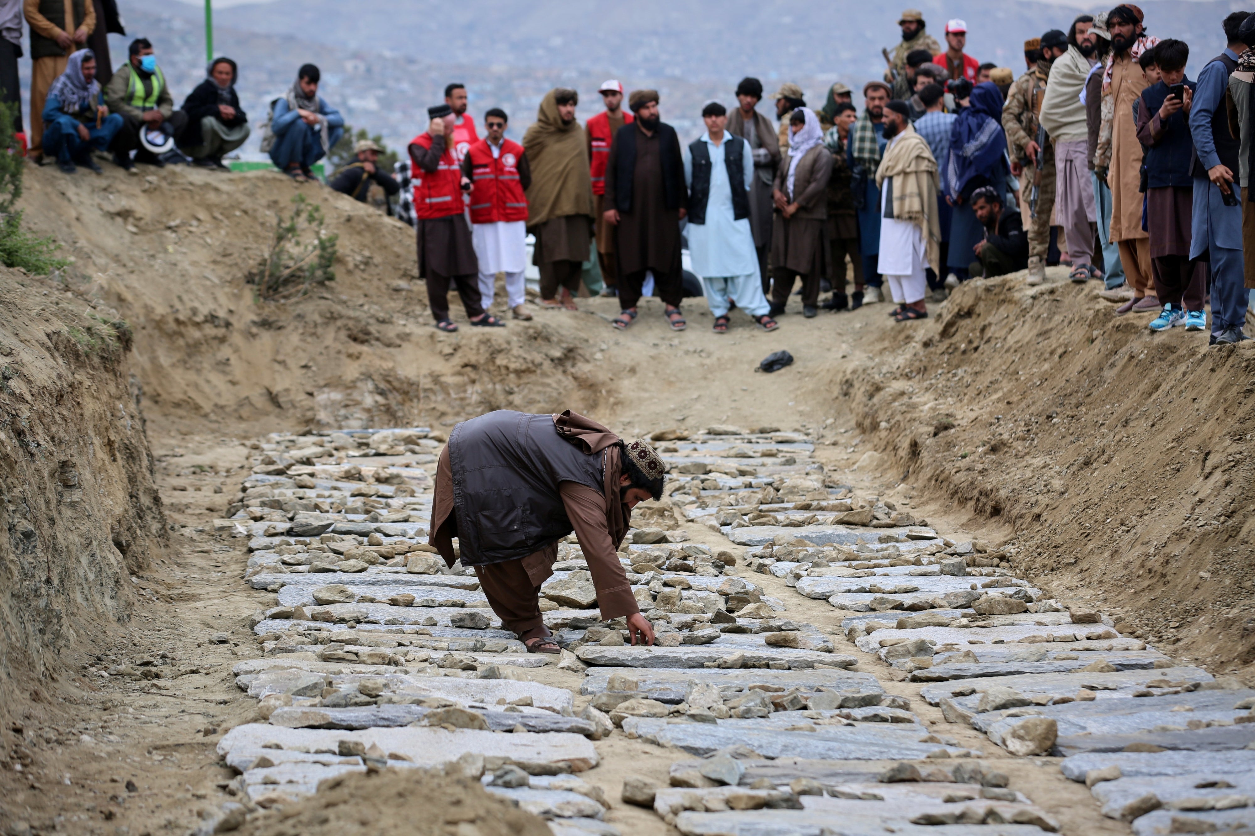 A man places stones on graves during a mass funeral for victims of the Pakistani  airstrike on the Omid drug rehabilitation center in Kabul, Afghanistan