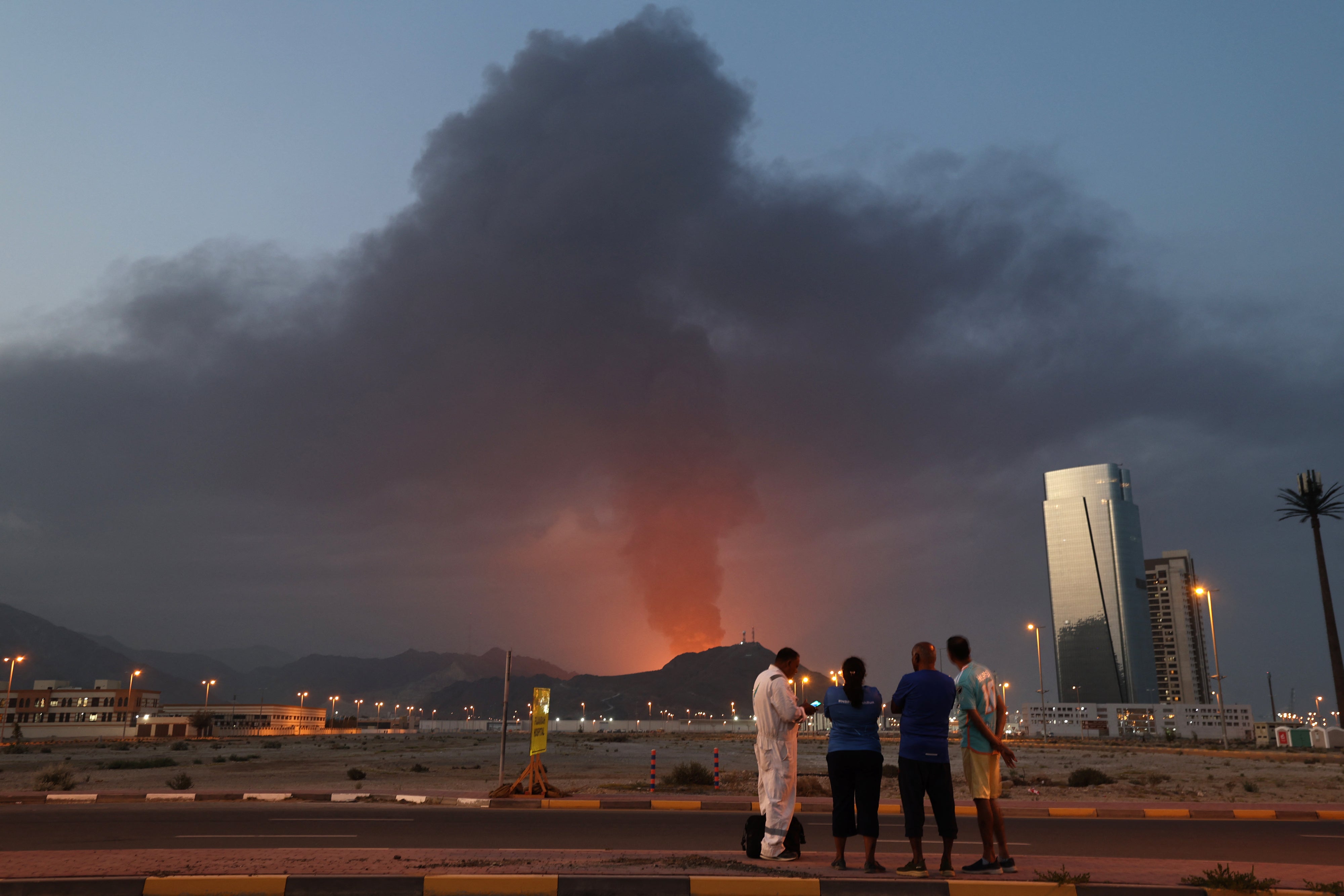 Foreign workers watch a plume of black smoke following an explosion in the Fujairah industrial zone in the United Arab Emirates, March 3, 2026. 