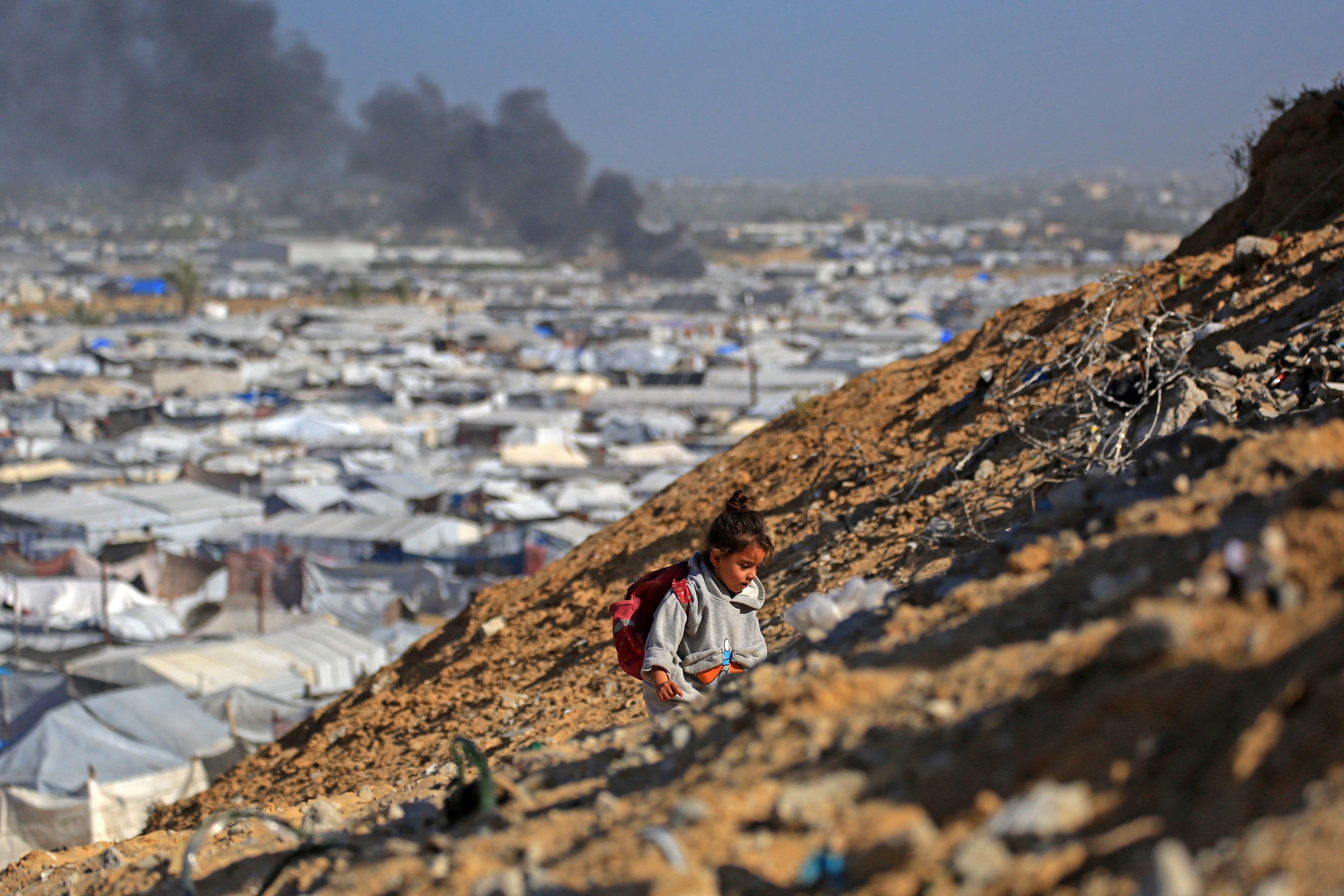 A girl climbs a hilltop against the backdrop of smoke rising from the Gath shelter, that houses displaced Palestinians, after an Israeli air strike in Khan Yunis, southern Gaza Strip on January 31, 2026. 