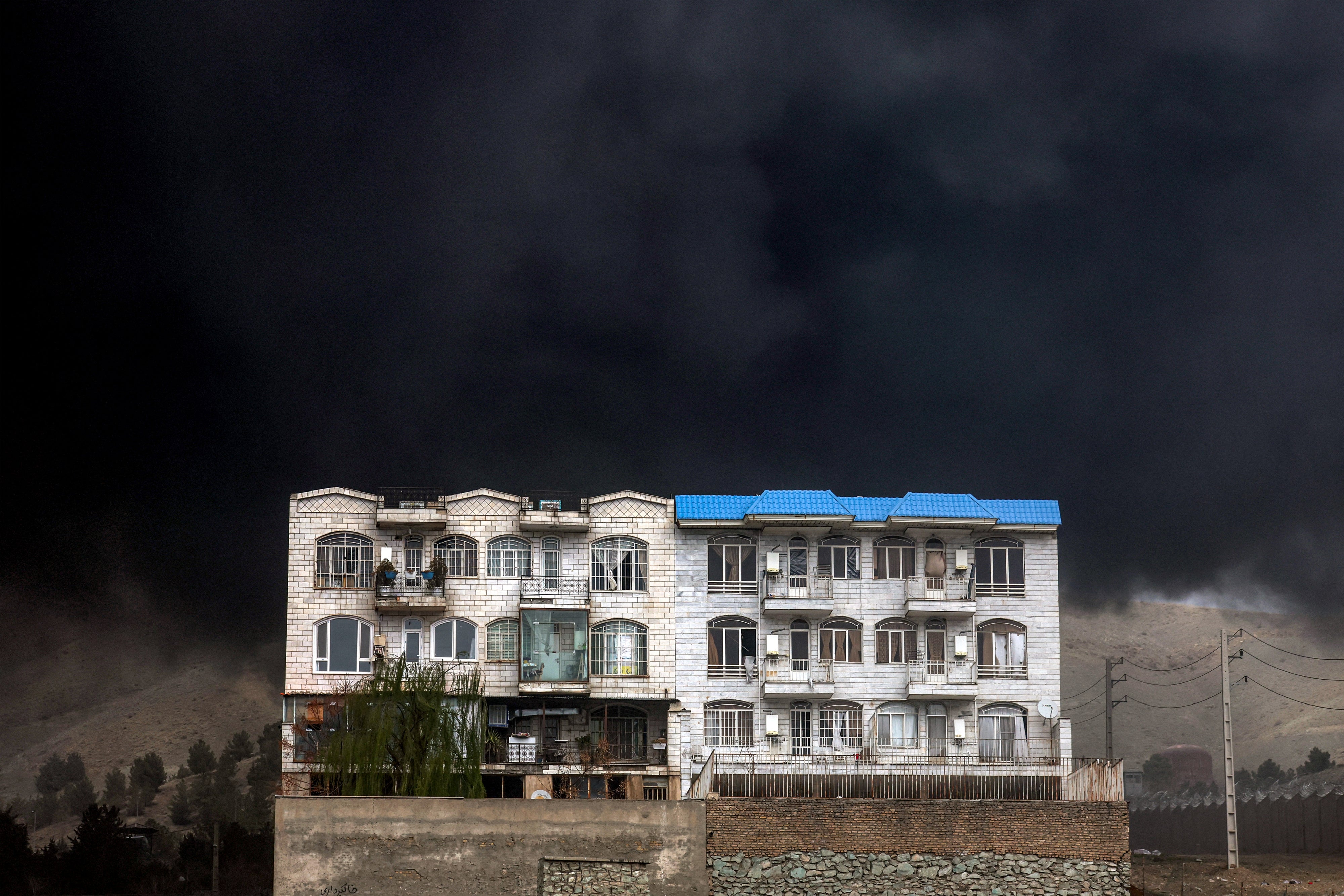 A dark smoke cloud engulfs a residential building near an ongoing fire following Israeli airstrikes on March 7, 2026 on the Shahran oil refinery in northwestern Tehran, Iran, March 8, 2026. 