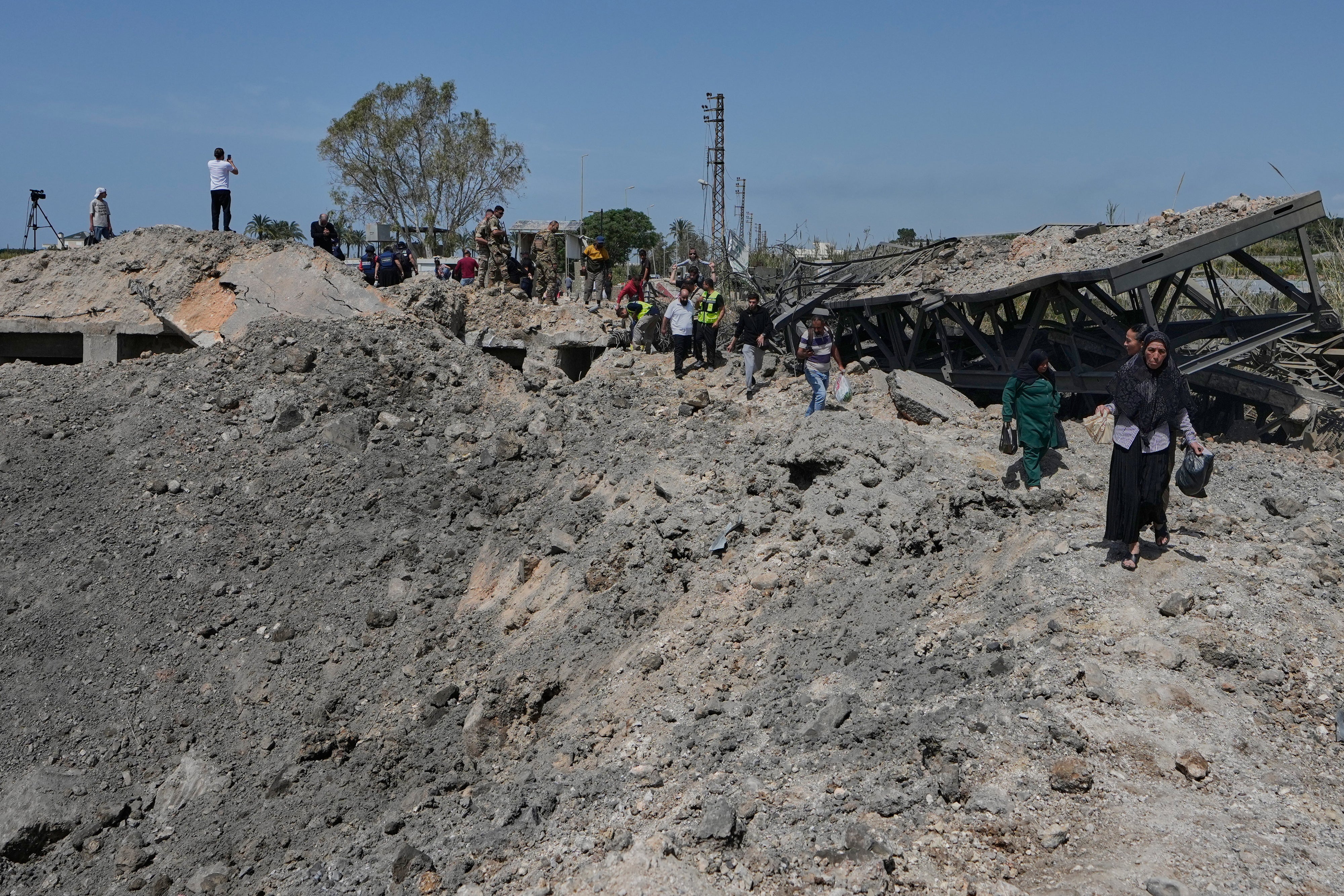 People cross on foot through a crater following an Israeli airstrike that destroyed the Qasmieh Bridge near the coastal city of Tyre, south Lebanon, April 16, 2026.