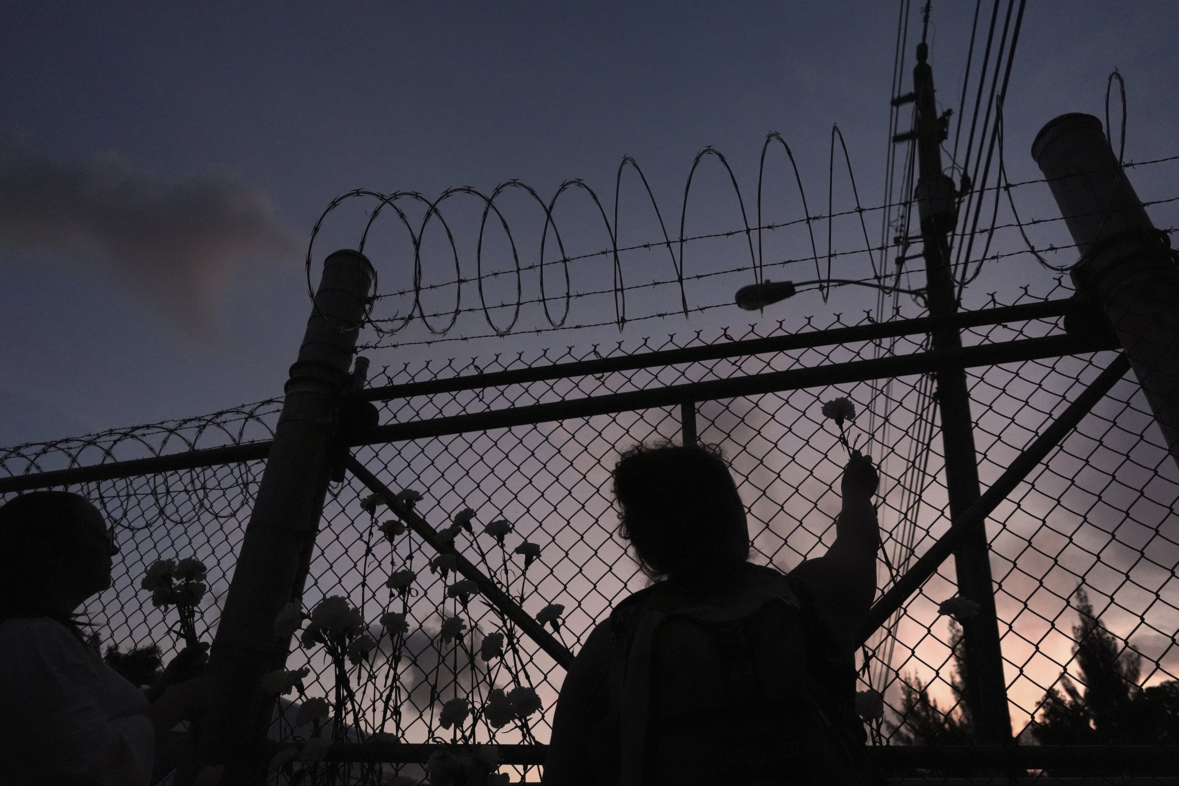 A woman places a flower on a fence outside Krome Detention Center
