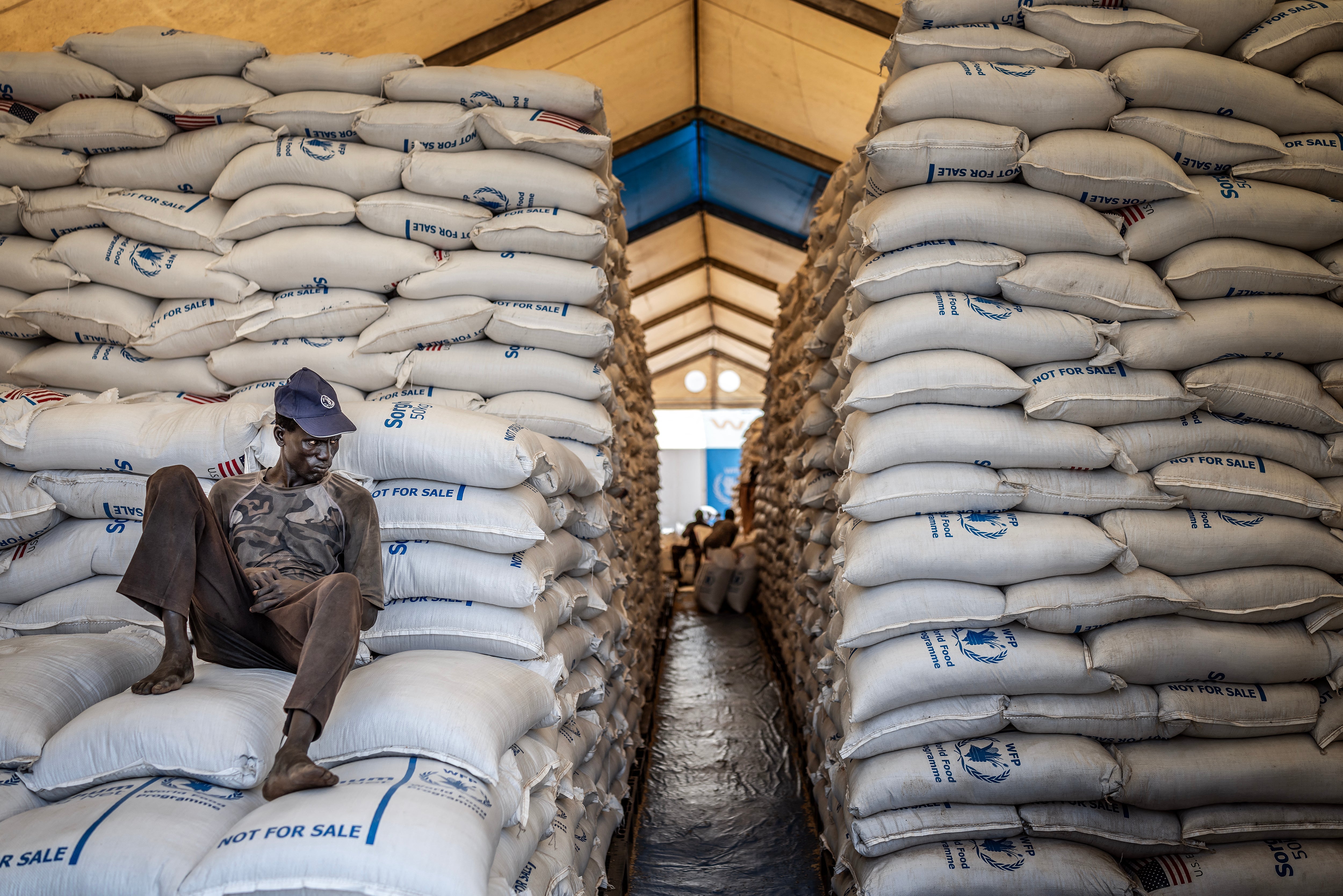 Un employé local du Programme alimentaire mondial (PAM) était assis sur des sacs de denrées alimentaire dans un hangar à Bor, dans l'État du Jonglei, au Soudan du Sud, le 13 février 2026 ; la livraison d’aide alimentaire dans cette région était bloquée en raison du conflit entre les forces gouvernementales et celles de l’opposition.