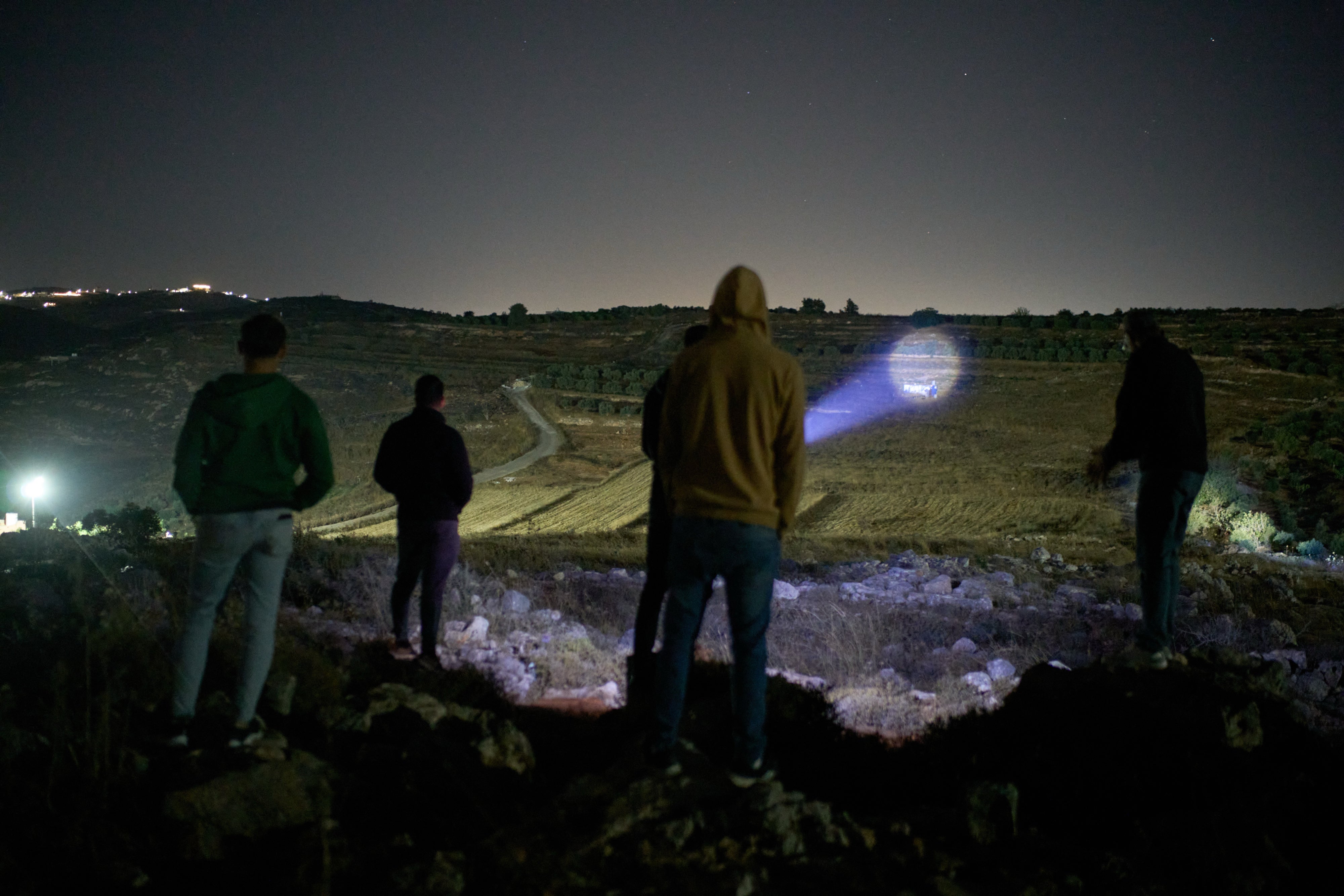 A Palestinian uses a flashlight on a nearby hill while taking part in a night watch with other volunteers to deter settler attacks on the West Bank village of Sinjil, July 16, 2026.
