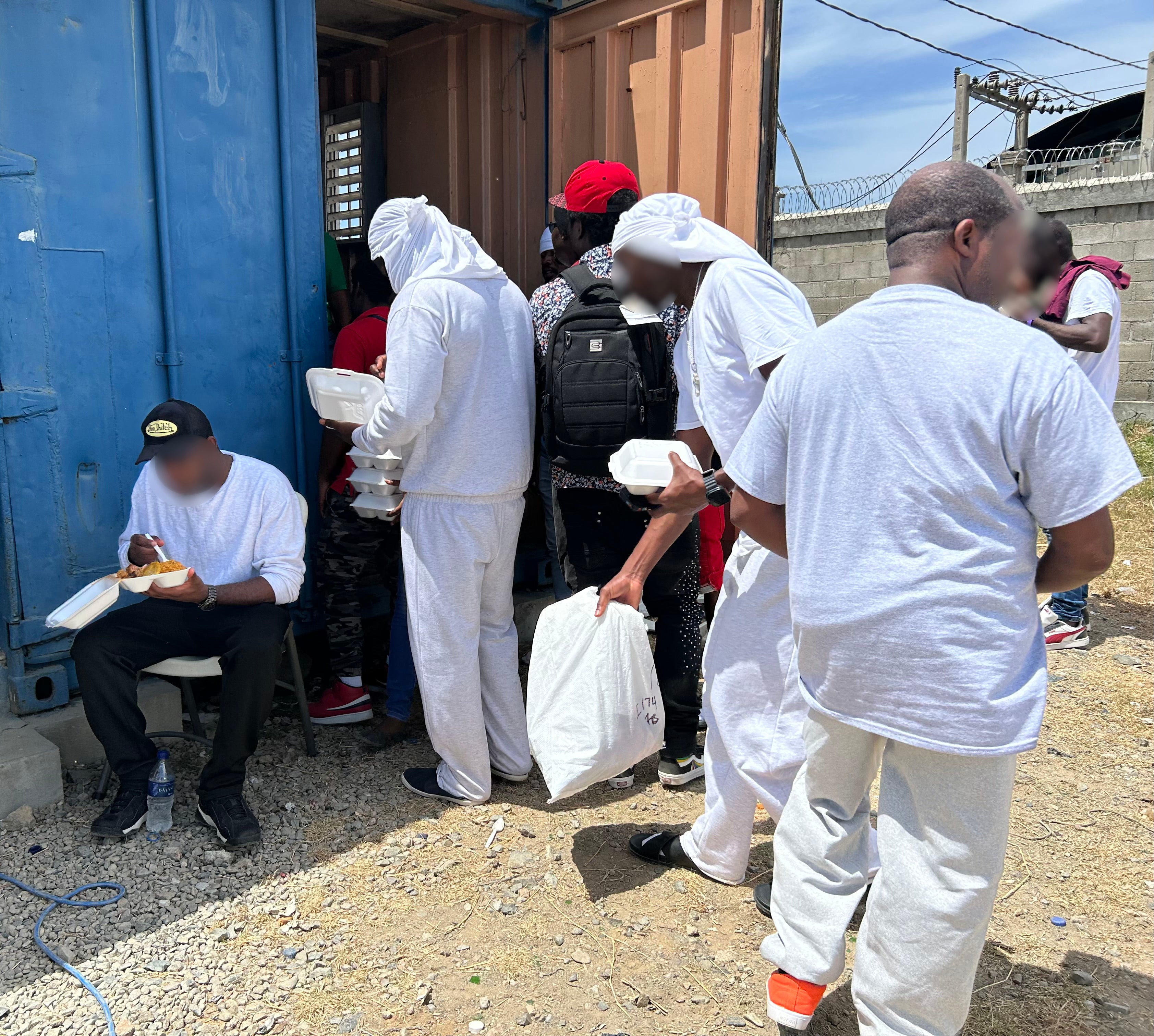 Haitian deportees receive meals outside the reception container at Cap-Haïtien International Airport, Haiti, August 27, 2026.