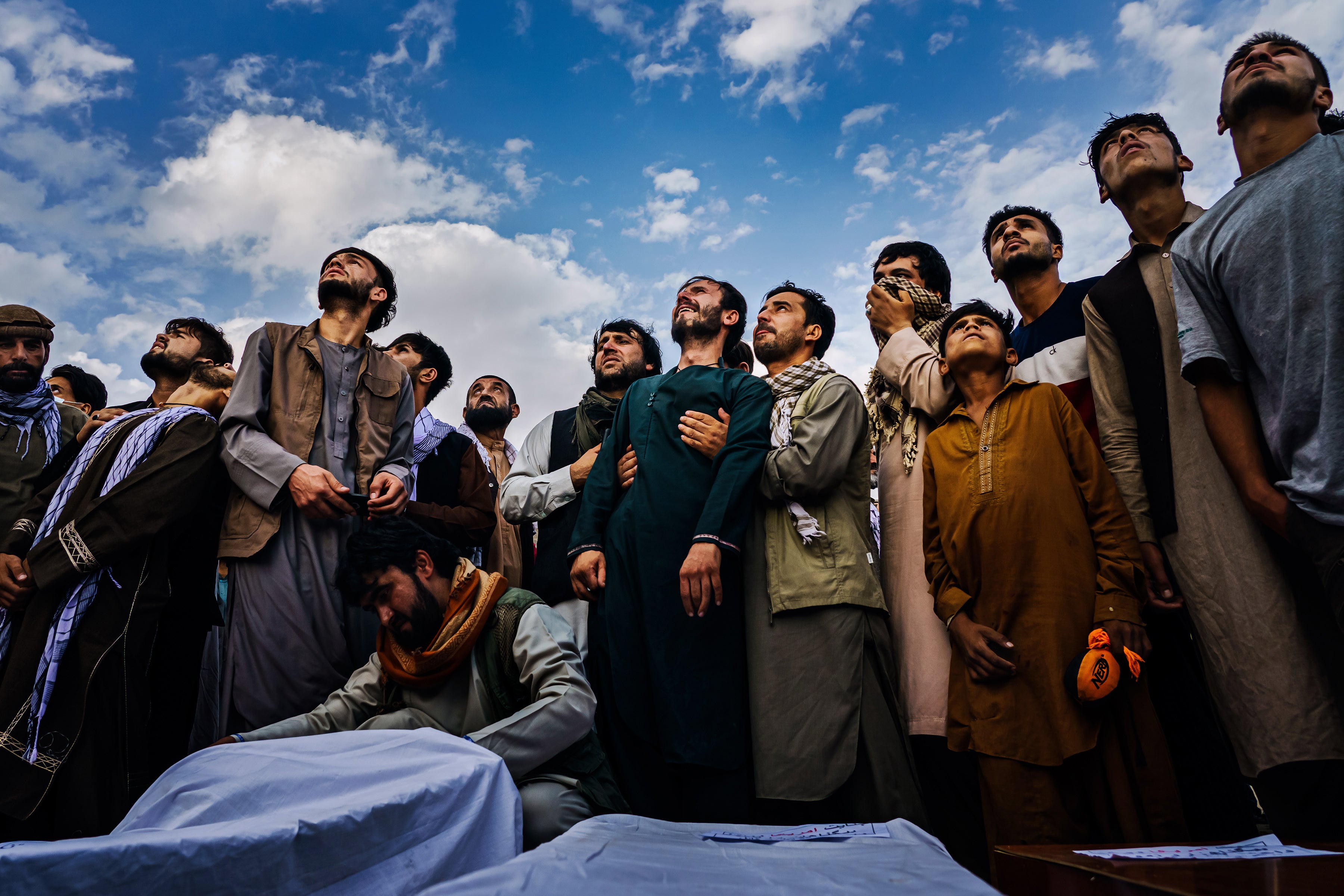 Mourners at a mass funeral for victims of a US drone strike, including seven children, look up as fighter jets circle a cemetery in Kabul