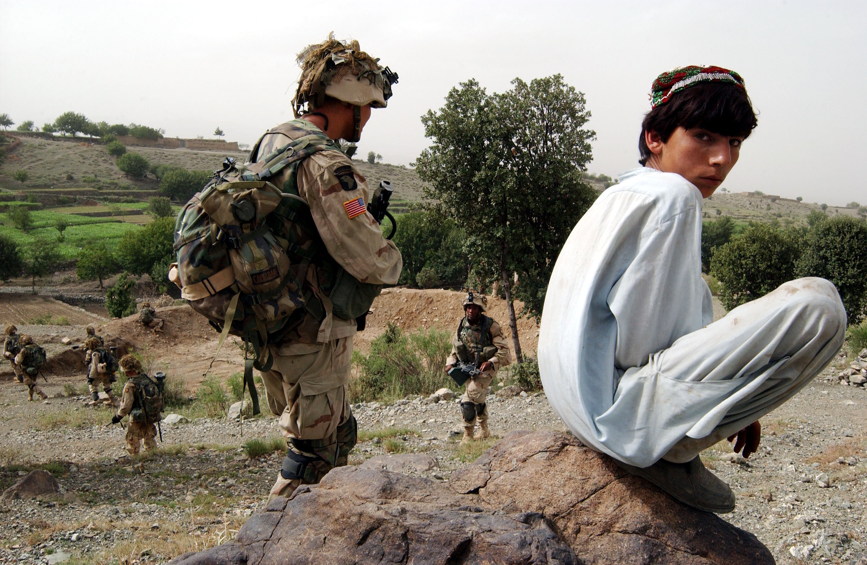 An Afghan boy watches as US Army 101st Airborne soldiers move in during a mission in southeastern Afghanistan, July 23, 2002. 