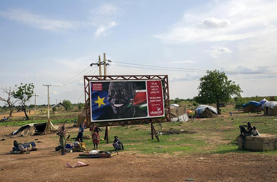 Civilians gather in front of a sign celebrating the second anniversary of South Sudan's independence as they prepare to flee from renewed attacks.