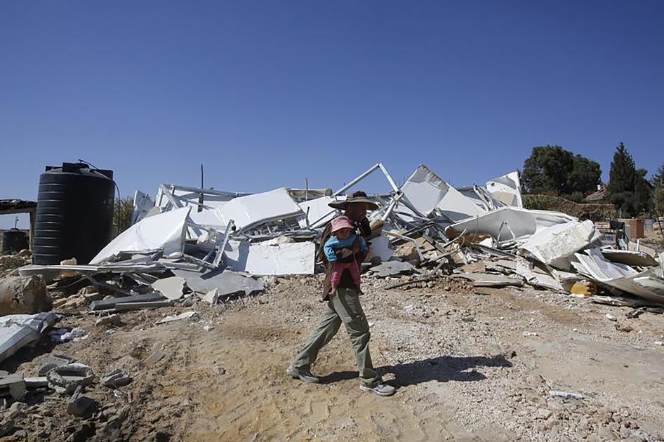 A Palestinian Bedouin carries his child as he walks past his caravan that was demolished by Israeli bulldozers near the Israeli settlement of Karmel, in the village of Um Alkhier near the West Bank city of Hebron October 27, 2014.