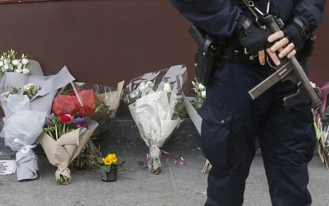 Un policier devant une rangée de bouquets déposés devant le restaurant Le Carillon à Paris, le 14  novembre 2015, au lendemain des attentats meurtriers commis dans la capitale.