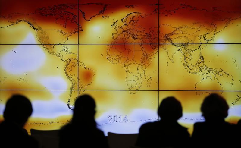 Participants are seen in silhouette as they look at a screen showing a world map with climate anomalies during the World Climate Change Conference 2015 (COP21).