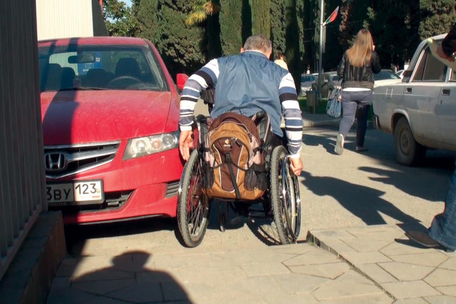 Alexander Simyonov navigates his wheelchair around a parked car in the Adler district of Sochi, February 8, 2013.