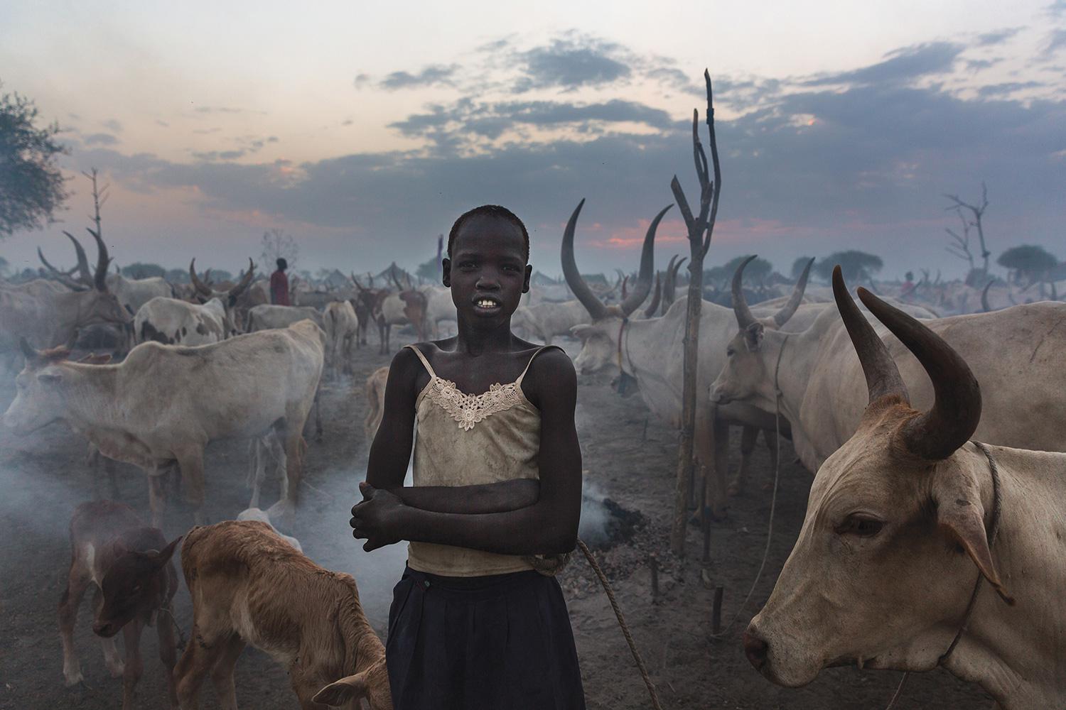 A young, unmarried girl stands amid a herd of cattle outside Bor, the capital of Jonglei State.  Cattle carry significant social, economic, and cultural importance for South Sudan's pastoralist ethnic groups, which use cows for payment of dowry.
