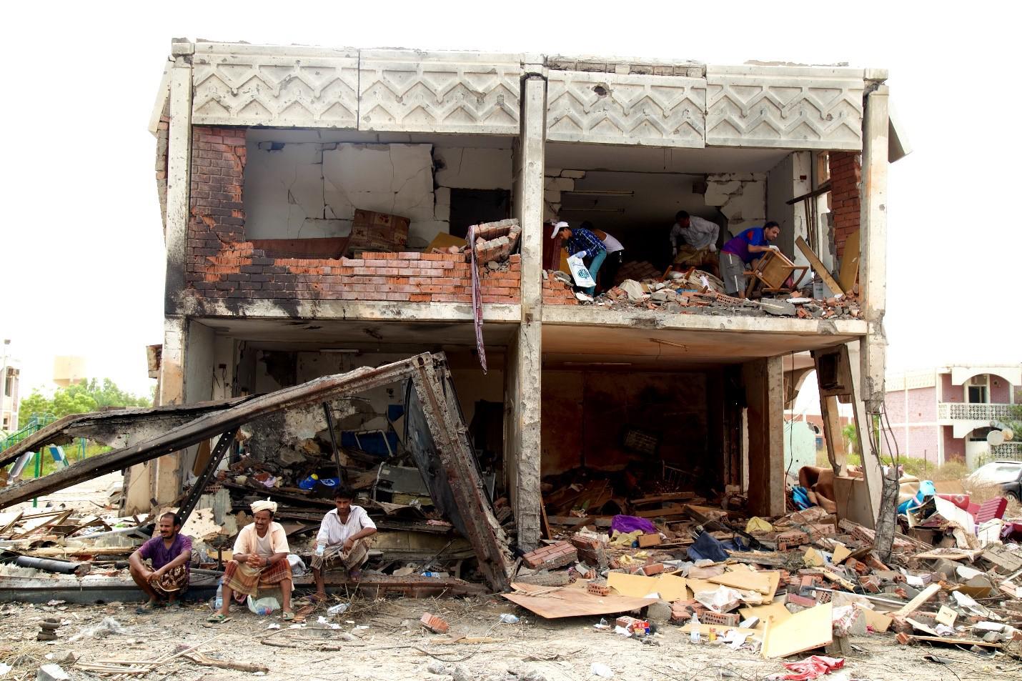 Des habitants de la ville côtière de Mokha, dans le sud-ouest du Yémen, assis devant les décombres de leur immeuble qui a été touché par une frappe aérienne ayant tué 65 civils, au surlendemain de l’attaque, le 24 juillet 2015, tandis que d’autres hommes 