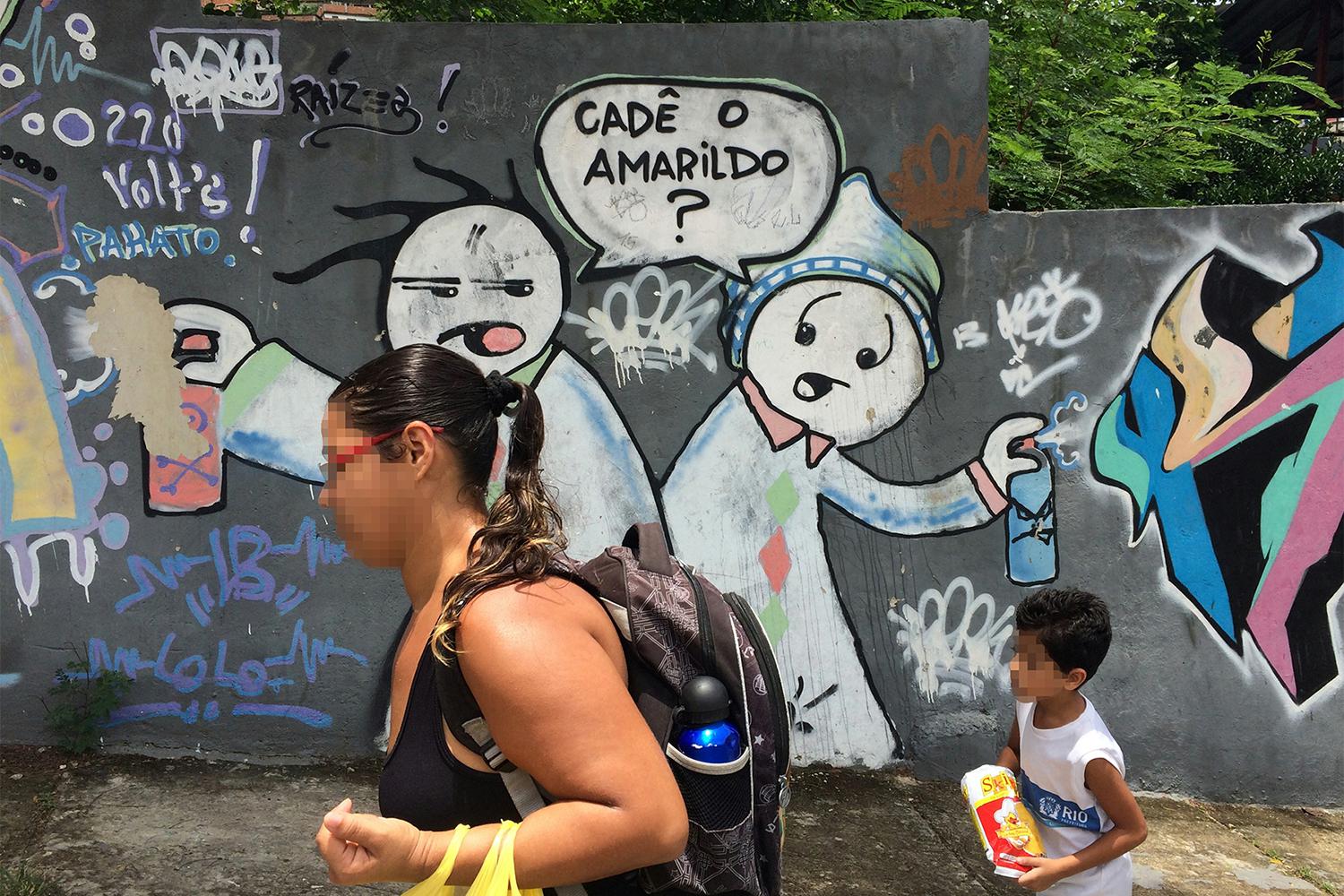 Two residents of theComplexo do Alemão favela walk on November 26, 2015 by graffiti that asks: “Where is Amarildo?” Amarildo de Souza, a 47-year-old construction laborer disappeared after police took him to the Pacifying Police Unit (UPP) at Rocinha favel