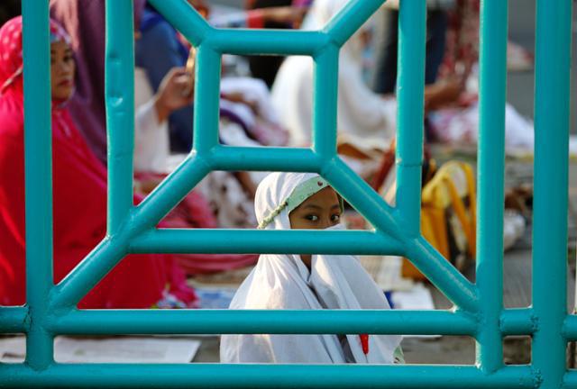 Seorang anak perempuan terlihat melalui pagar sebelum salat hari raya Idul Adha bagi umat muslim di sebuah jalan di Jakarta, Indonesia 12 September 2016. 