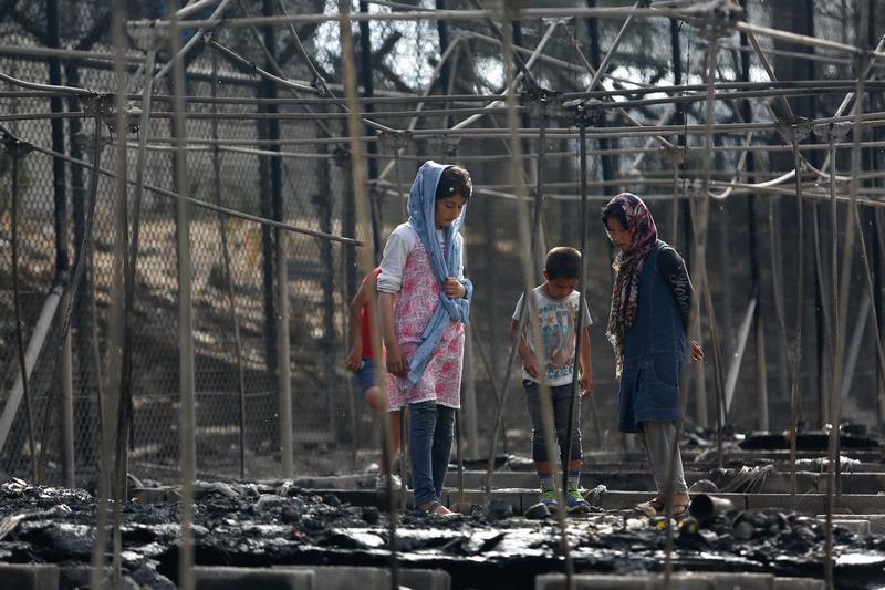 Migrants stand among the remains of a burned tent at the Moria hotspot, after a fire ripped through tents and destroyed containers on the island of Lesbos, Greece, September 20, 2016.