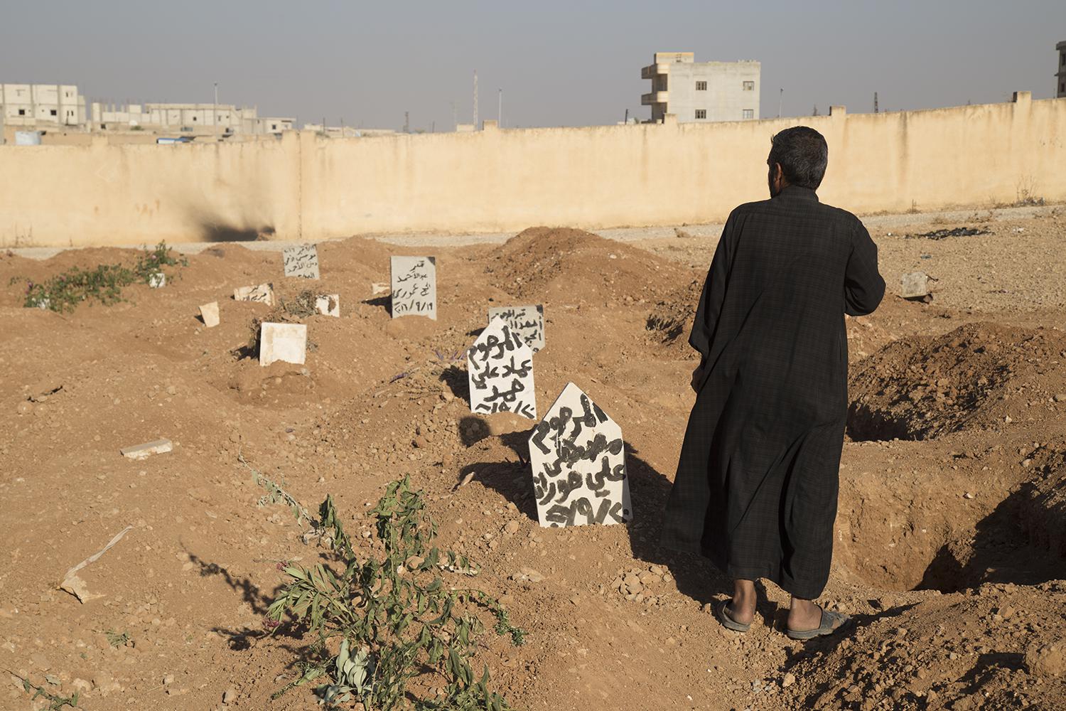 يقف أحد أفراد العائلة أمام قبور 3 أطفال قُتلوا بانفجار عبوة ناسفة زرعها داعش في مدرسة في منبج يوم 27 سبتمبر/أيلول 