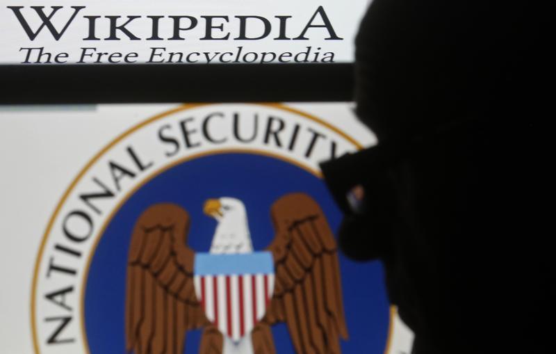 A man is silhouetted near logos of the U.S. National Security Agency (NSA) and Wikipedia in this photo illustration taken in Sarajevo March 11, 2015.