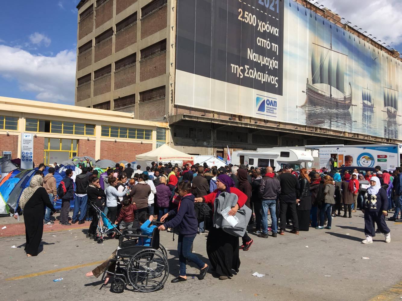 Asylum seekers and migrants at a makeshift camp at the port of Piraeus, queuing for distribution of survival kits by the Hellenic Red Cross. In the absence of any visible government support or personnel the day to day operation of the camp is dependent on