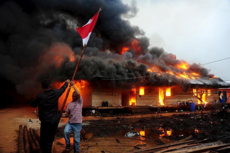 Dua lelaki mencabut bendera Merah Putih ketika lahan pertanian komunitas Gafatar dibakar di kabupaten Mempawah, Kalimantan Barat, pada 18 Januari 2016.