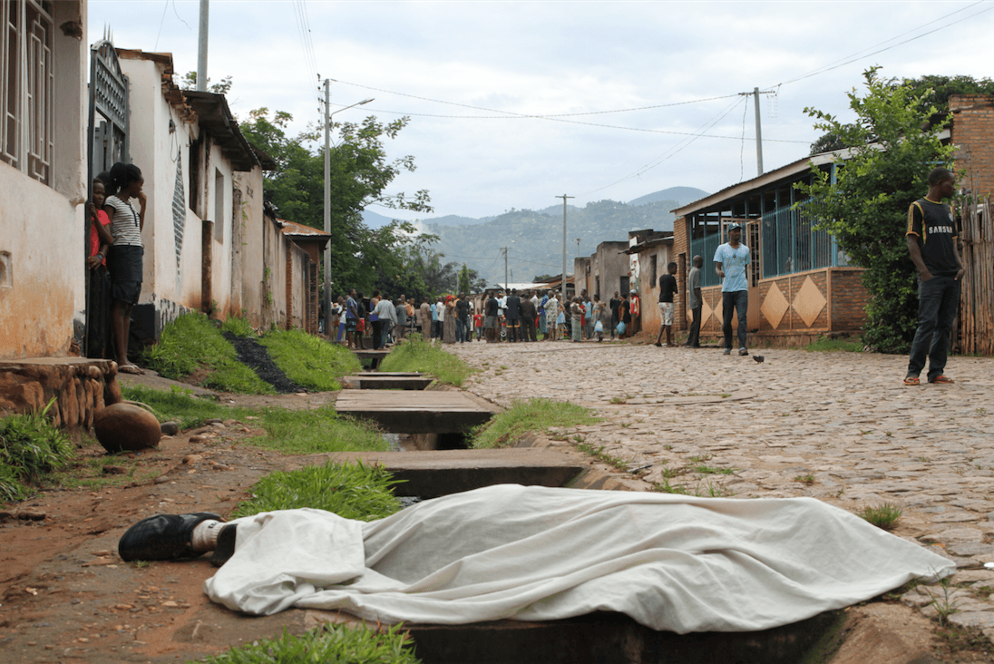 Residents outside their houses in Nyakabiga, in the Burundian capital Bujumbura, look at the body of a man shot dead on December 11, 2015.