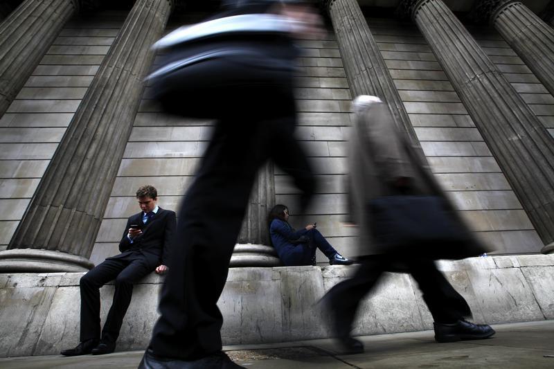 A man and woman use their mobile phones as commuters walk past the columns of the Bank of England in the City of London, July 3, 2012. 