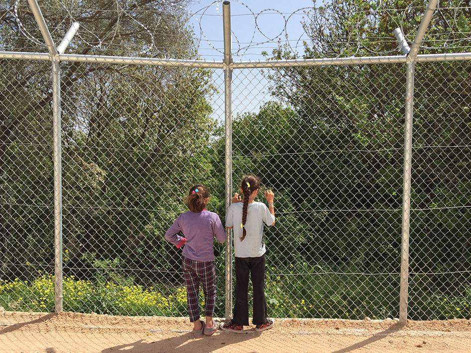 Deux jeunes filles migrantes regardent une forêt jouxtant le centre de détention de VIAL, sur l’île grecque de Chios, à travers le grillage du centre, en avril 2016.