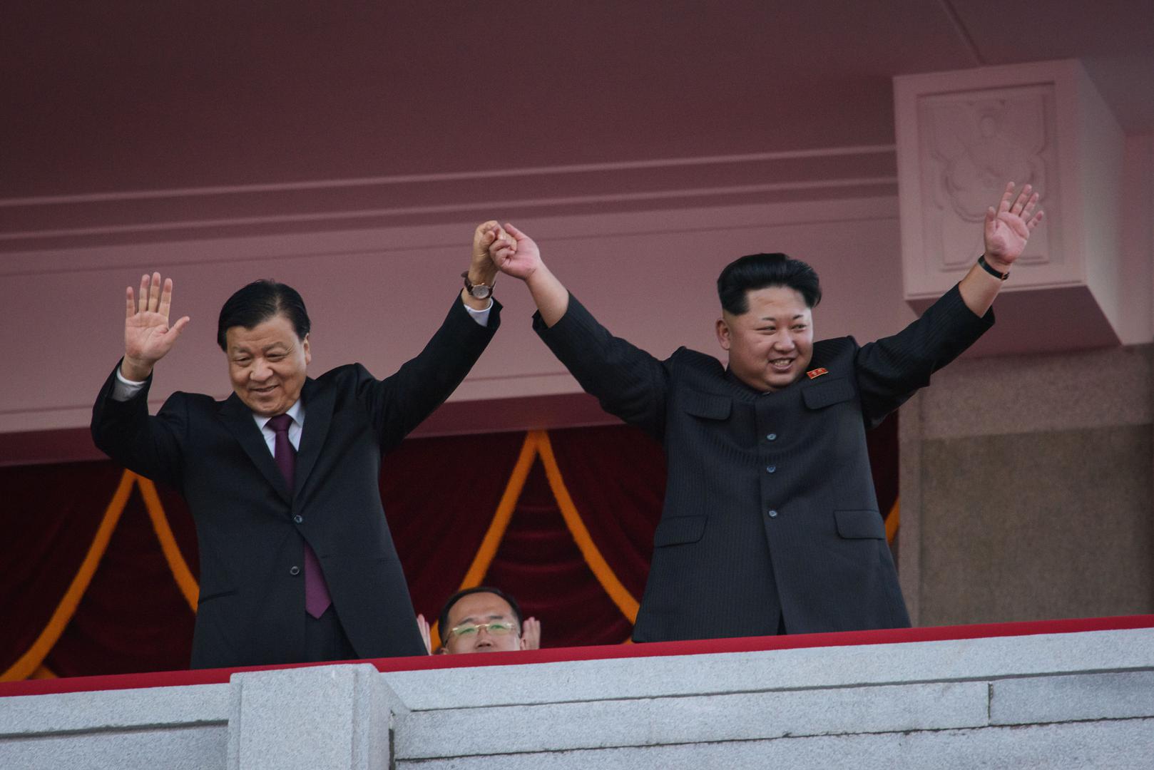 North Korea's leader Kim Jong-Un (R) and Chinese Politburo standing committee member Liu Yunshan (L) wave from a balcony towards participants of a mass military parade at Kim Il-Sung square in Pyongyang on October 10, 2015