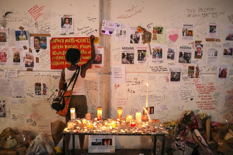A woman writes on a wall covered with tributes to and pictures of the victims of the Grenfell apartment tower fire in North Kensington, London, Britain, June 18, 2017.