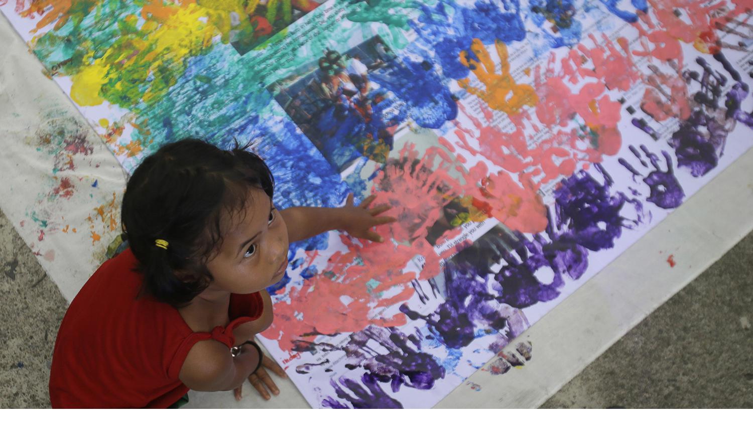 A girl covers anti-LGBT messages in rainbow handprints during a Pride rally in Manila on June 27, 2015. 