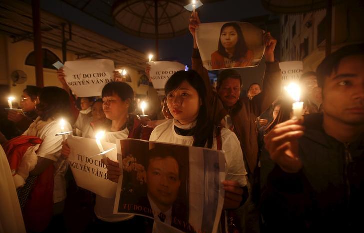 武明庆（中）捧着丈夫阮文大相片，她身边的天主教友则手持腊烛和阮文大助手黎秋荷的相片，参加河内泰和教会为两人举办的祈福弥撒，2015年12月27日。