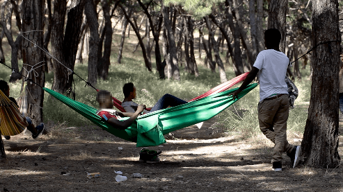 “Amadou,” a 16-year-old unaccompanied boy from West Africa standing by two other people in hammocks in Lesbos, Greece.