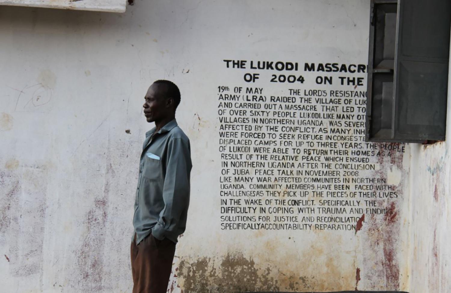 A community member in Lukodi stands next to a memorial of a May 19, 2004 massacre, one of the atrocities for which Dominic Ongwen is facing charges before the International Criminal Court. Over 4,000 victims are participating in the trial. 
