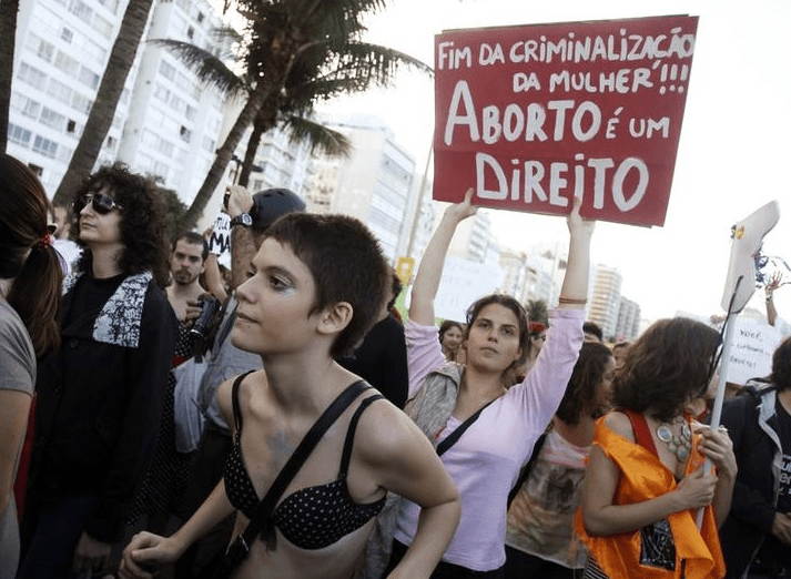 Pessoas participam da manifestação "Marcha das Vadias" na praia de Copacabana, no Rio de Janeiro, onde o Papa Francisco celebrou uma missa à noite, em julho de 2013. No cartaz está escrito "Fim da criminalização da mulher. Aborto é um direito"