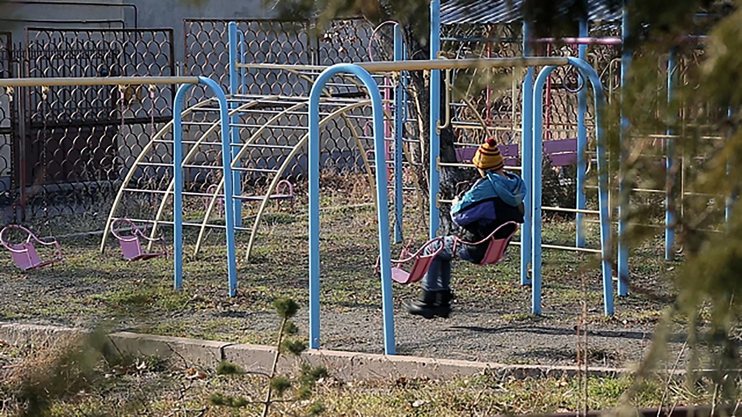 Մի տղա նստած է ճոճանակին հաշմանդամություն ունեցող երեխաների համար նախատեսված մանկատան բակում, Երևան, Հայաստան: 