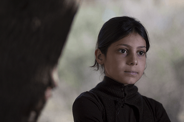 براءة (10 أعوام)، من الغوطة الشرقية، تقف أمام شجرة نصبت عليها لوحا في المخيم غير الرسمي حيث تقيم في جبل لبنان، وبدأت بتعليم الأطفال الأصغر سنا ما تتذكره من الصف الأول عندما كانت في سوريا. 