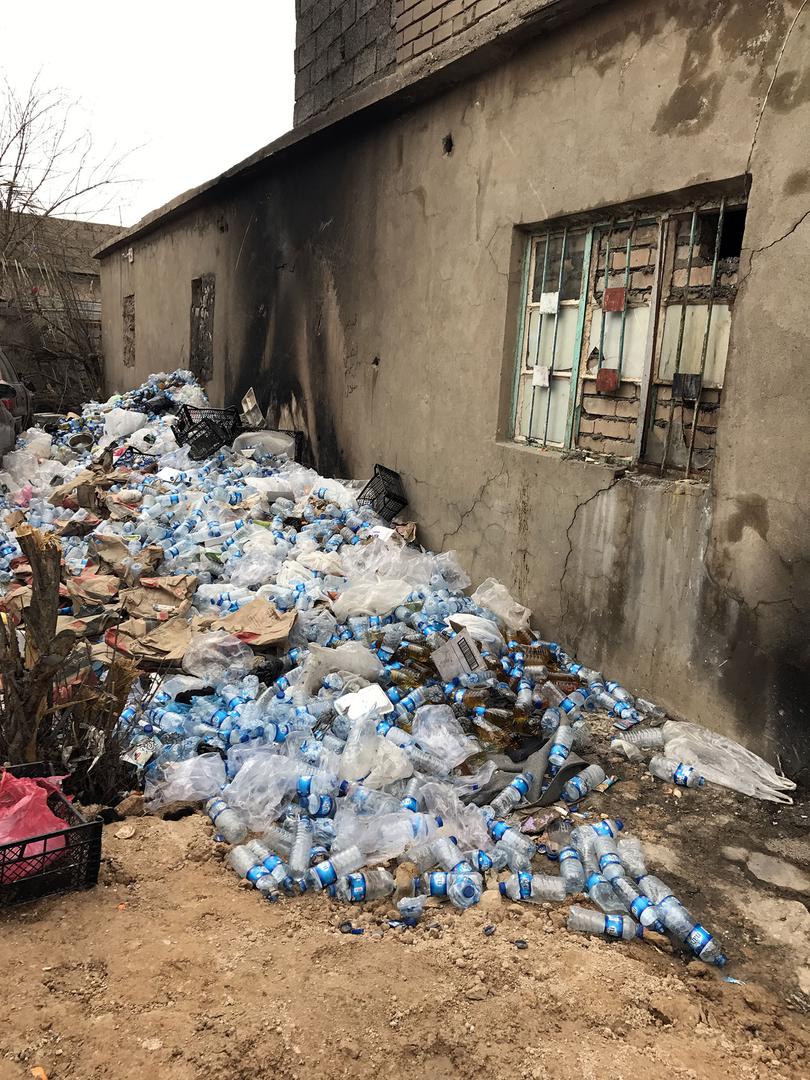 A pile of water bottles filled with urine outside a hole in the wall from a 3x4 meter cell holding 38 detainees. 