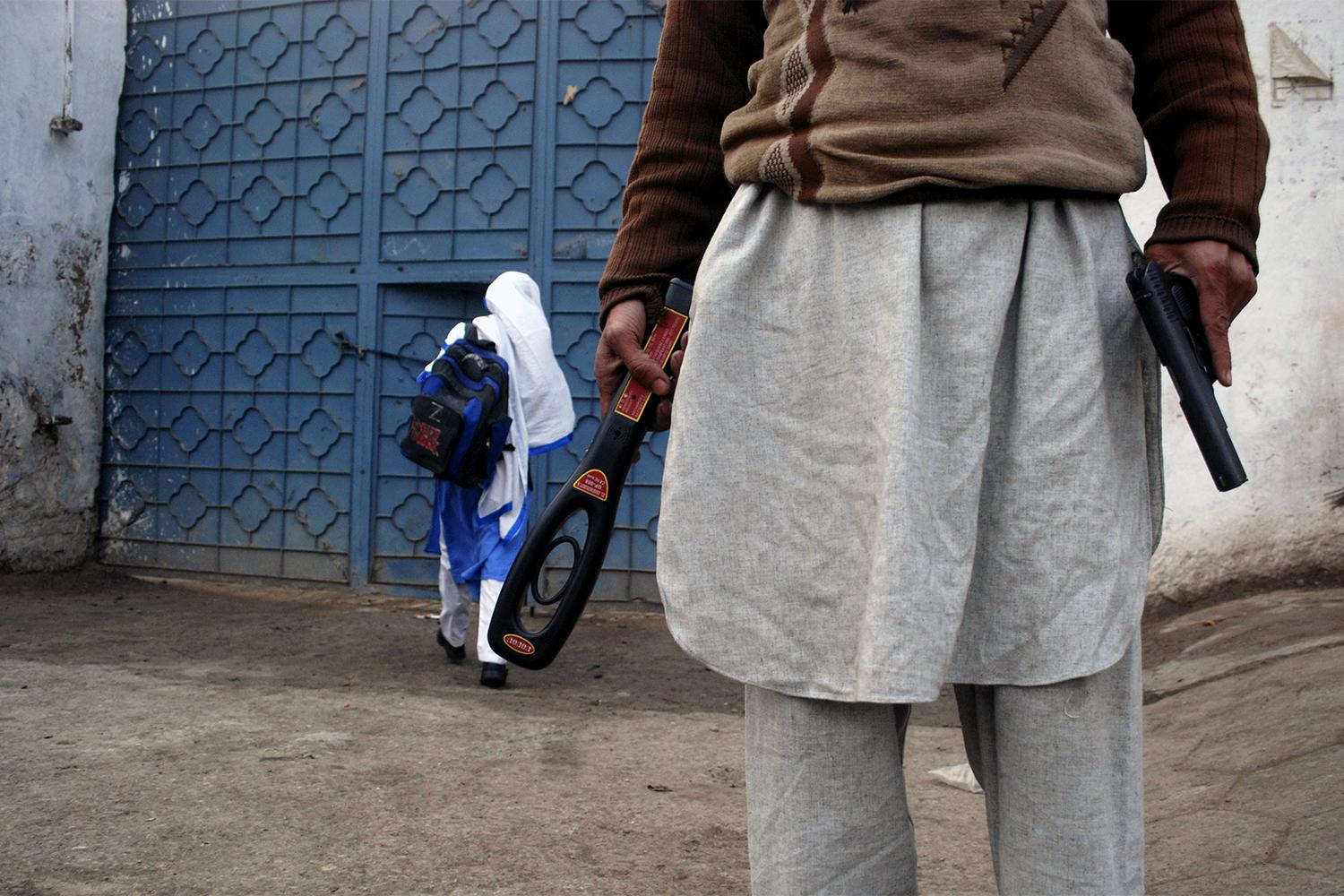 A guard with a gun and a metal detector stands outside a school after it reopened in Peshawar, January 2015.