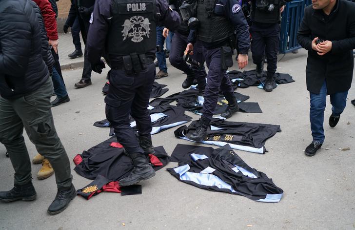 Ankara Üniversitesi’nin Cebeci Kampüsünde, akademisyenlerin üniversitelerden ihraç edilmesini protesto etmek amacıyla yapılan eylemde çevik kuvvet polisleri yere serilen cüppeleri ayaklarının altında ezerek yürüyorlar.