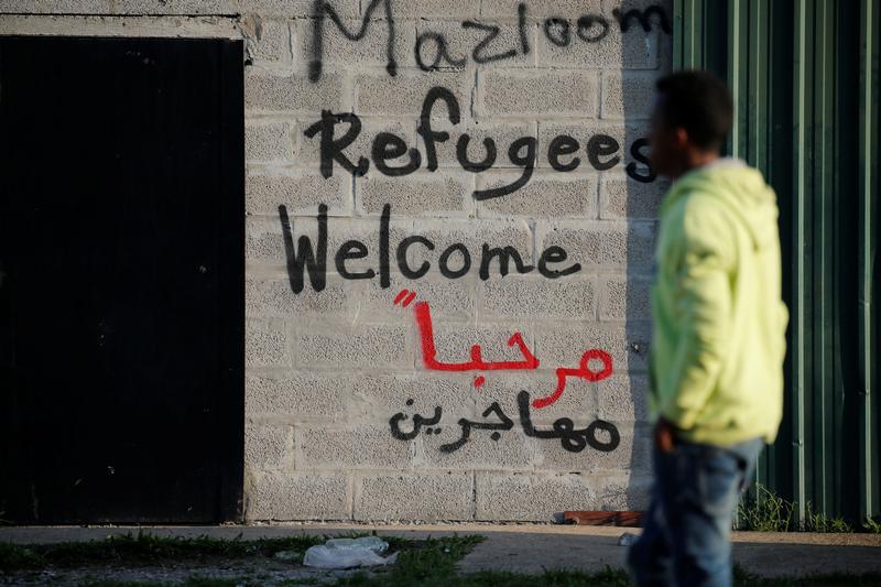 un migrant passe devant les slogans “Refugees Welcome” (réfugiés bienvenue) écrits sur un mur près de l’ancienne « Jungle » à Calais, France, le 23 août 2017