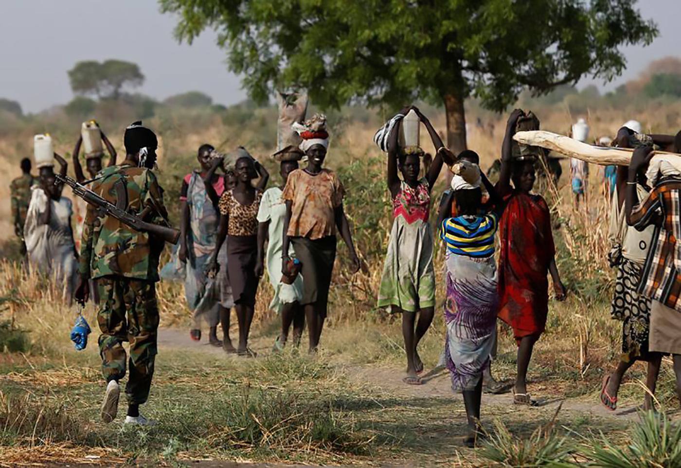 A soldier walks past women carrying their belongings near Benitu, northern South Sudan, February 11, 2017. 