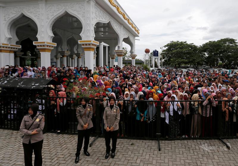 Indonesian police women guard people who watch a man publicly flogged.