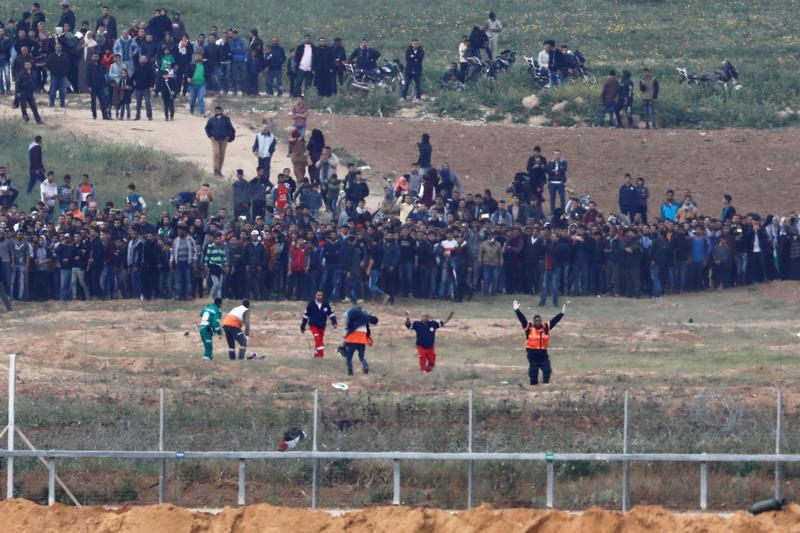 مسعفون فلسطينيون يخلون رجلا على جانب غزة من السياج الذي يفصل القطاع عن إسرائيل، كما يبدو المشهد على الجانب الإسرائيلي من الحدود، خلال مظاهرات 30 مارس/آذار بمناسبة "يوم الأرض". © 2018 رويترز