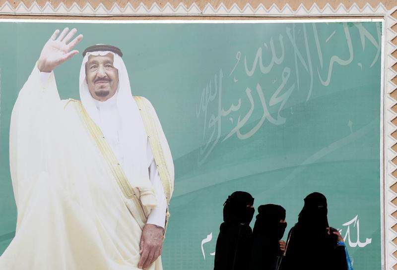 一群妇女经过沙特阿拉伯国王萨勒曼画像，沙特阿拉伯利雅得，2018年2月12日。