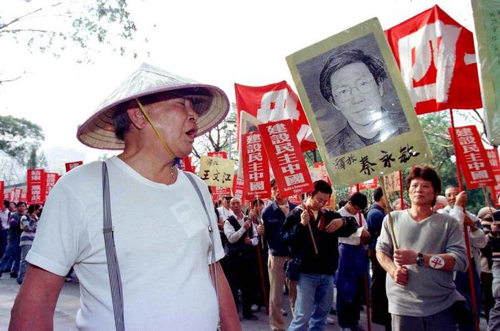 一名亲中共人士（左）大声辱骂即将出发游行的民主派示威群众，香港，1999年1月1日。这次游行是民主派人士为纪念六四天安门屠杀十周年所发起的系列活动第一场。图右示威民众手举中国民运人士秦永敏照片。