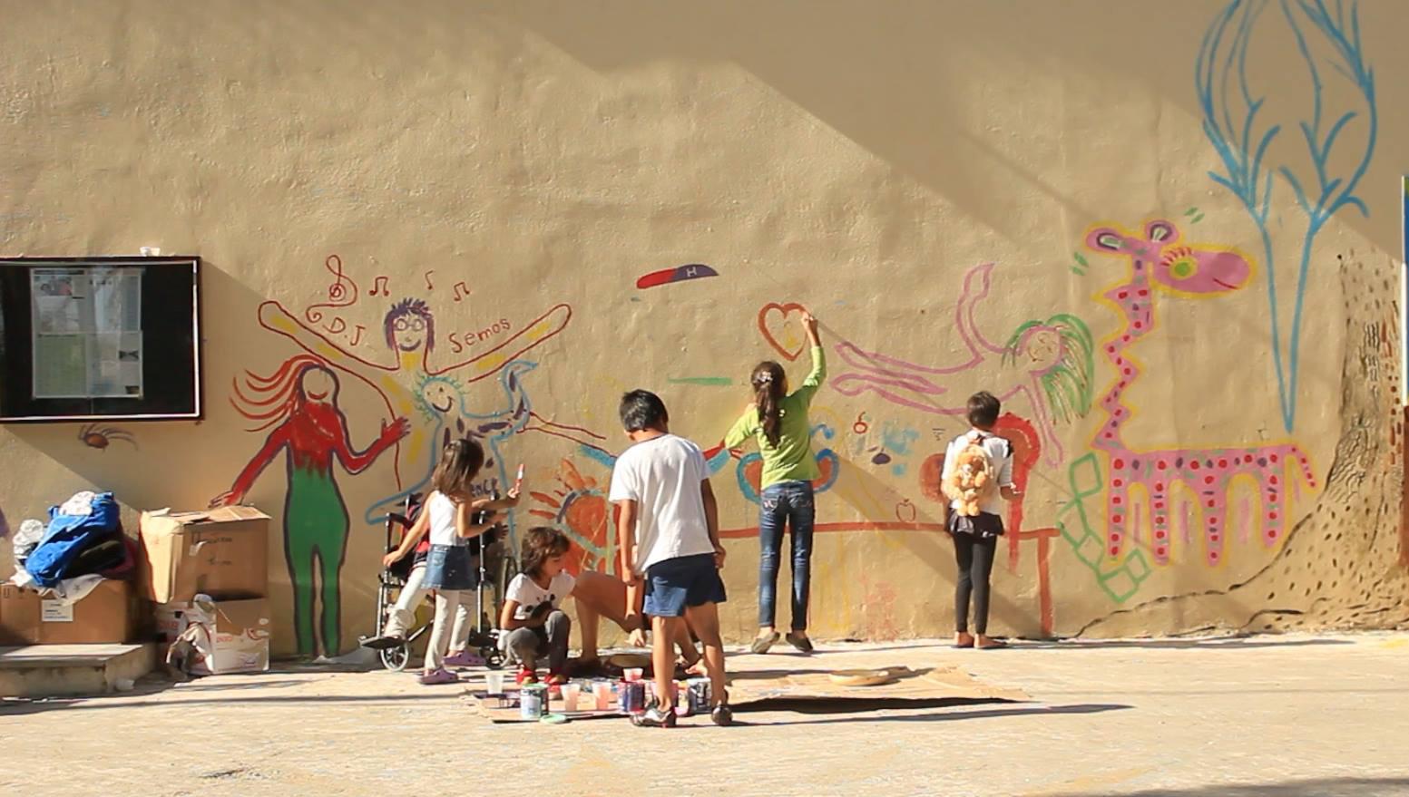 کودکان در پیکپا، کمپ پناهجویان در جزیرۀ لسبوس، دیواری را تزئین میکنند. مددکاران به کودکان کمک میکنند که آنها برای