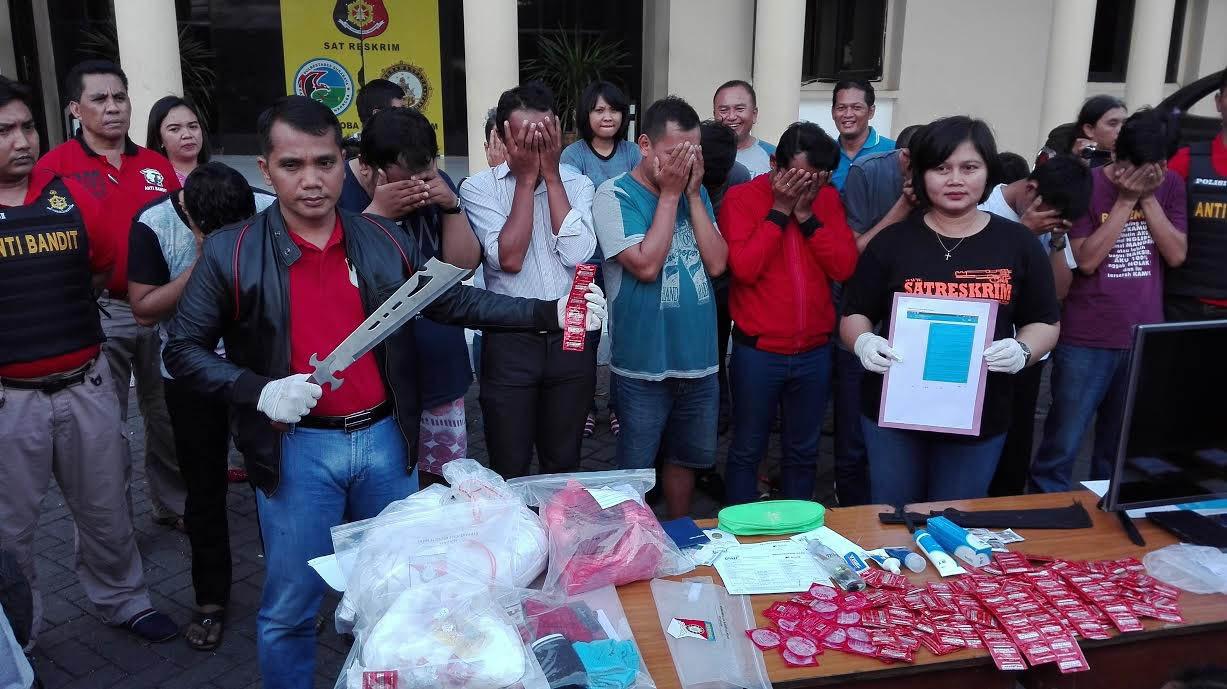 Authorities show condoms, lubricant, and HIV test results to the media while detainees cover their faces after police raided a hotel room in Surabaya.