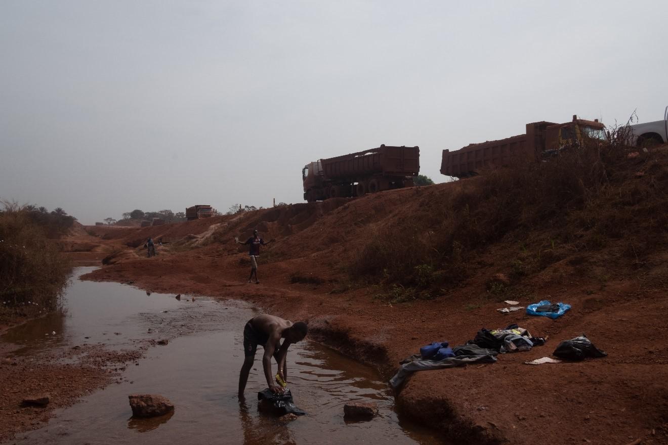 A man washes clothes next to a mining road belonging to the La Société Minière de Boké (SMB) consortium.